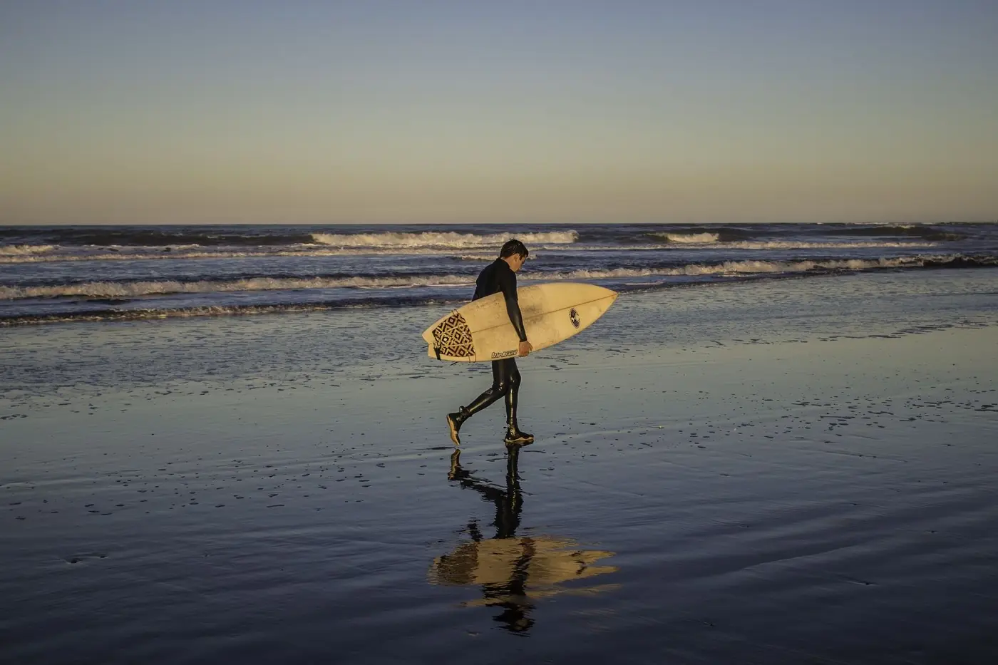 Surfer walking the tideline at sunset